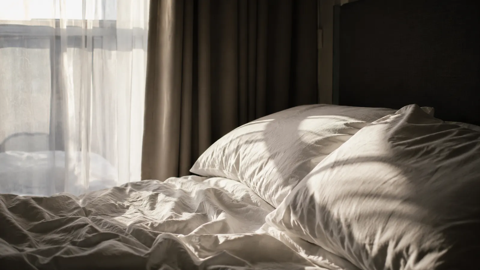 Bright early morning sunlight streaming through a bedroom window, illuminating a pillow and sheets