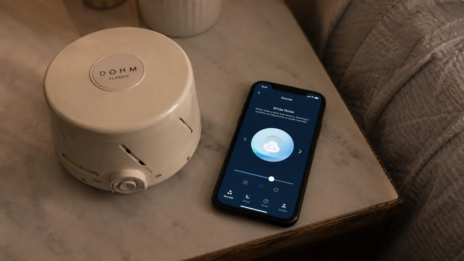 Yogasleep Dohm Classic next to a phone showing a white noise app, contrasting the physical machine with a digital alternative